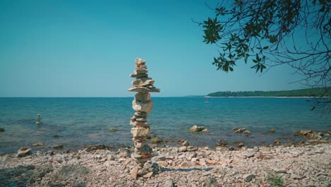 Cinemagraph---seamless-video-loop-of-a-giant-stone-tower-at-a-romantic-beach-at-the-Croatian-Mediterranean-seaside-with-a-SUP-stand-up-paddle-board-standing-still-in-the-clean-and-clear-blue-water