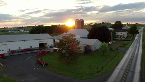 Establishing-shot-of-small-American-family-farm,-barn,-buildings,-silos-at-sunrise-sunset-with-dramatic-flare-effect