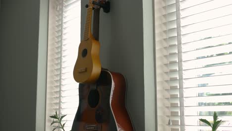 Two-guitars,-a-large-and-a-small,-hanging-in-the-house-on-the-wall-between-two-louvered-windows