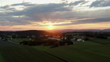 Aerial-push-in-dolly-shot-of-sunrise,-sunset-in-Lancaster-County-Pennsylvania,-rolling-hills-and-green-farmland-during-summer,-beautiful-clouds-and-sky,-panorama