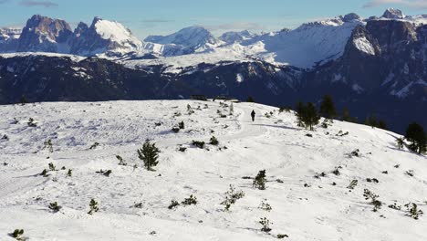 Lone-hiker-walking-toward-the-massive-peaks-of-the-snow-capped-mountains-of-the-Dolomites-in-a-winter-wonderland-of-Rittner-Horn-near-Bolzano,-Italy