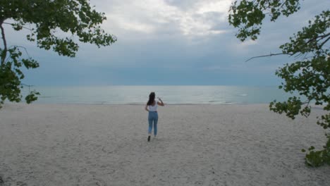 Woman-walking-away-from-the-camera-on-the-cloudy-beach-in-Prince-Edward-County,-Ontario,-Canada