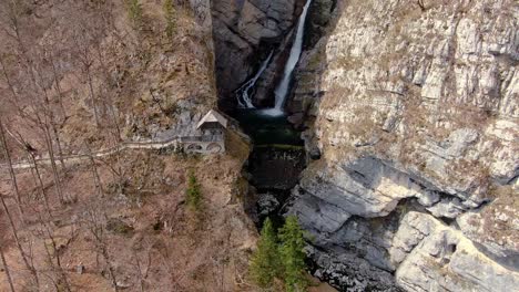Aerial-showing-spectacular-waterfall,-hidden-amidst-the-steep-walls-of-the-brown-rocky-mountain-in-Bohinj,-Slovenia
