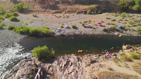 Auburn-swimming-hole-on-American-River-in-California-surrounded-by-green-trees-and-filled-with-people-swimming-and-enjoying-their-summer-weekend---Drone-flying-backwards