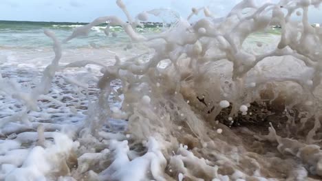 The-sea-wave-crashing-into-a-small-rock-on-a-sandy-beach-slow-motion-clip