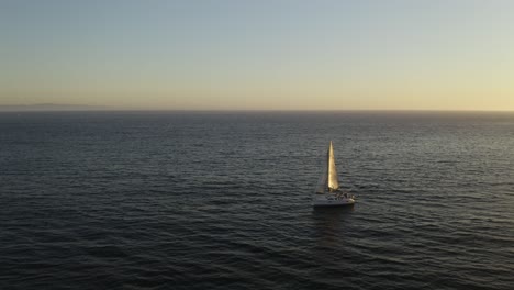 Drone-Reveals-Yacht-Blowing-in-Wind-Alone-at-Sea,-Sunset-on-Ocean