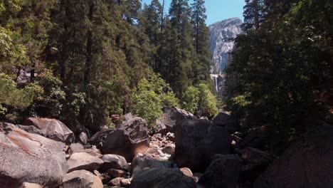 Slow-handheld-shot-of-piles-of-large-granite-boulders-in-a-dried-up-river-with-a-waterfall-in-the-background