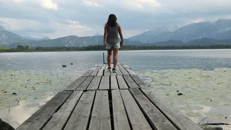 Woman-Walking-Down-a-Wooden-Jetty-at-Lake-Hopfensee-near-Fuessen-Enjoying-the-Scenery,-Bavaria,-Germany