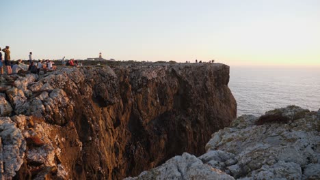 Establishing-shot,-People-gathering-near-the-edge-of-a-Rocky-cliff-in-on-Algarve,-Portugal,-Scenic-view-of-the-Sea-and-Sun-rise-in-the-background