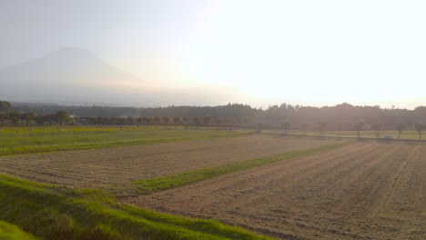Left-rotating-aerial-shot-over-agricultural-fields-with-tall-silhouette-of-Mount-Fuji-in-distance