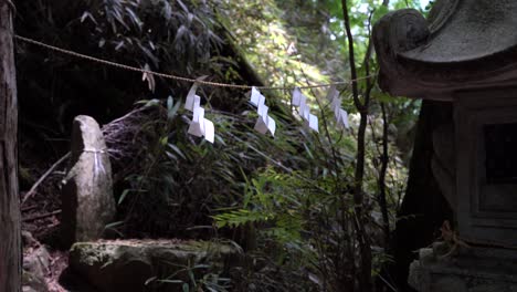 White-paper-tied-on-rope-against-Japanese-stone-pillars-in-forest---Locked-off-view
