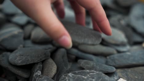 Female-hand-picking-up-flat-rock-on-beach,-slow-motion-close-up