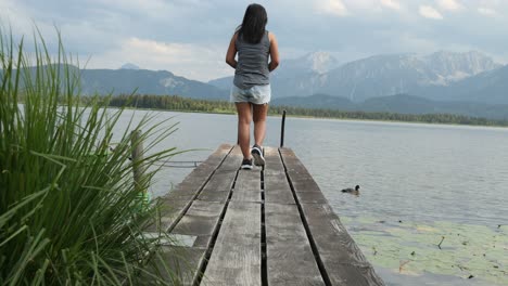 Mujer-Caminando-Por-Un-Embarcadero-De-Madera-En-El-Lago-Hopfensee-Cerca-De-Fuessen-Disfrutando-Del-Paisaje,-Baviera,-Alemania