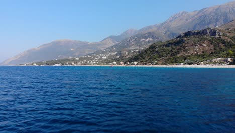 Blue-sea-horizon-bordered-by-sandy-beach-and-mountain-landscape-on-touristic-villages-in-Albania