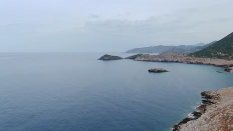 Aerial-Over-Calm-Waters-Beside-Rocky-Coastline-In-Crete