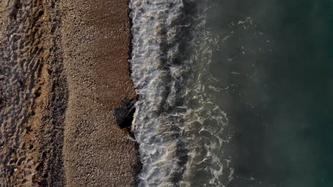 Sea-waves-splashing-on-big-cliff-covered-by-pebbles-on-remote-beach-of-Mediterranean-coastline