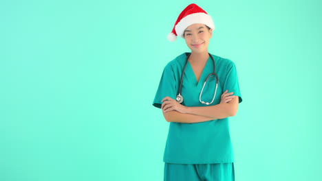 Enfermera-Médica-Asiática-Sonriente-Con-Sombrero-De-Santa-Claus-Y-Estetoscopio-De-Servicio,-Aislada-En-Un-Fondo-Turquesa