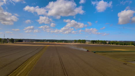 A-Farm-Machinery-Harvesting-Crops-In-A-Vast-Field-In-Puck,-Poland-On-A-Summer-Day---aerial-drone---wide-shot