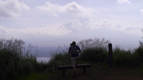 Männlicher-Wanderer,-Der-Auf-Die-Bank-In-Der-Nähe-Des-Mt-Fuji-Klettert-Und-In-Die-Ferne-Blickt