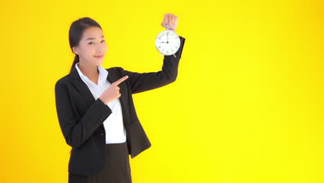 A-young-businesswoman-on-a-solid-background-raises-a-clock-then-points-to-it