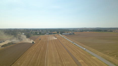 Farm-Machines-Harvesting-Ripe-Crops-At-The-Field-In-Kielno,-Poland-With-Vehicles-On-The-Road---descending-drone-shot