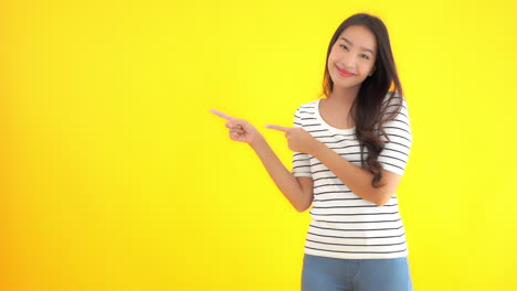 Attractive-asian-female-with-long-hair-in-striped-dress-pointing-with-fingers-on-left-side,-static-slow-motion