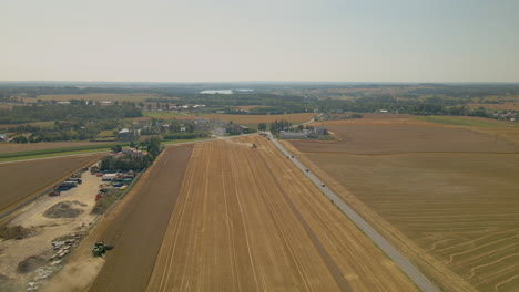 Beautiful-Farm-Landscape-In-Kielno,-Poland-By-The-Road-With-Tractors-Harvesting-On-A-Hot-Sunny-Weather---descending-drone-shot