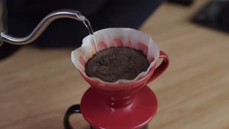 Pouring-hot-water-from-pot-into-red-coffee-filter-cup-cone-with-coffee