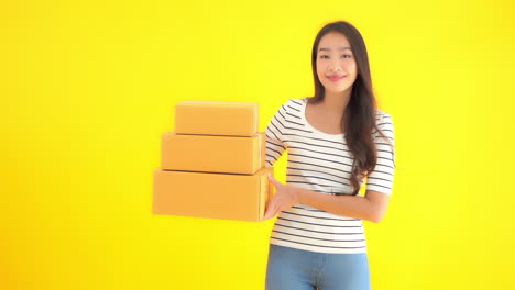 Young-woman-holding-three-unmarked-boxes-in-front-of-solid-yellow-background