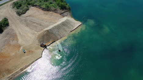 Steady-aerial-view-of-excavator-moving-around-and-and-stones-at-the-lakeside