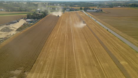 Long-And-Winding-Road-Between-Broad-Farmlands-In-Kielno,-Poland-With-Tractors-Harvesting-Crops-On-A-Sunny-Day---aerial-drone---pullback-shot