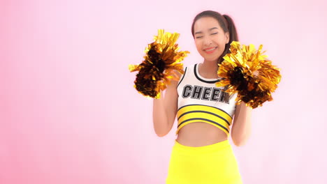 A-cute-cheerleader-in-a-uniform-smiles-while-she-shakes-her-sparkly-pom-poms
