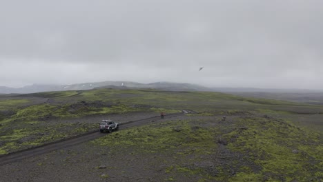 Una-Bicicleta-Seguida-Por-Un-Coche-Conduciendo-Por-La-Carretera-De-Montaña-En-Islandia-En-Un-Día-De-Niebla---Drone-Aéreo