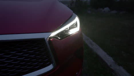 Epic-Closeup-Shot-of-a-Red-Car-with-Chrome-Detail-and-Black-Grille-with-Modern-LED-Headlight-on-during-a-Cold-Slightly-Foggy-Night,-Crane-Down-with-Tilt-Up