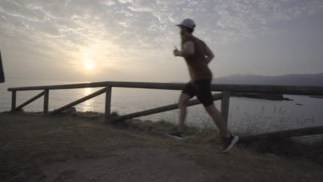 Man-running-in-nature,-ocean-at-the-background,-sunrise,-cloudy-day,-static-shot