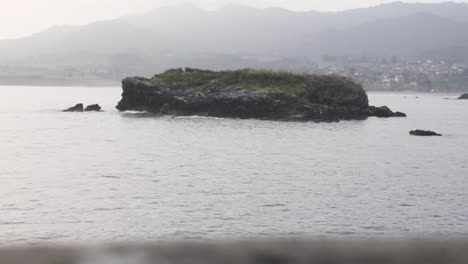 Kleine-Insel-Mitten-Im-Ozean,-Berge-Im-Hintergrund,-Asturien,-Spanien,-Statische-Aufnahme