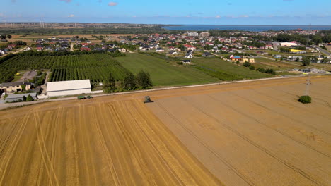 Drone-Approaching-An-Agricultural-Harvesting-Machinery-At-Work-On-The-Wheat-Field-In-Puck,-Poland---aerial-tilt-down