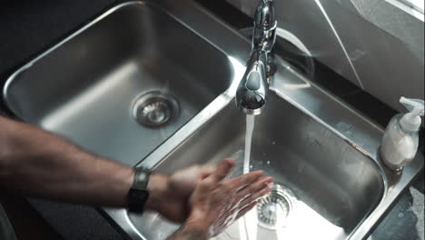 Hands-Wearing-Watch-Turn-on-Tap-of-Stainless-Steel-Basin-and-Wash-Hands-Surgically-with-Soap-According-to-COVID-19---Coronavirus-Guidelines,-Close-Up-Shot