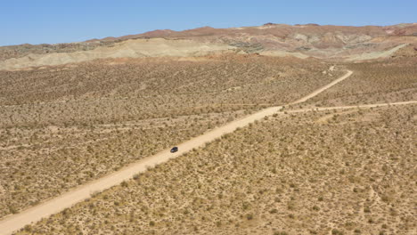 Dark-black-SUV-drives-down-a-straight-dirt-road-going-through-a-wide-open-desert-landscape