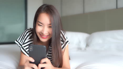 Close-up-of-a-young-attractive-woman-texting-on-her-smartphone-while-lying-on-a-big-comfy-bed