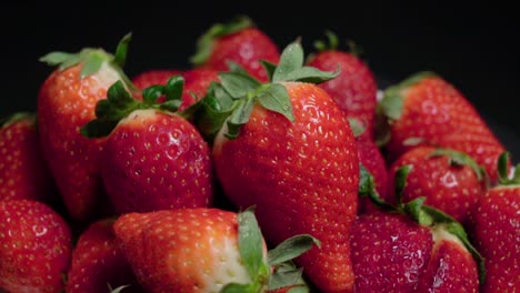 Bright-Red-Strawberries-Piled-on-Black-Background,-Closeup-Tilt-Down-Shot