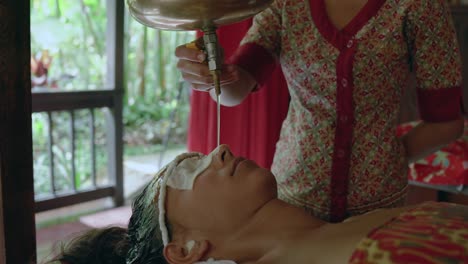 Woman-relaxes-in-a-private-room-while-receiving-a-stress-relieving-Shirodhara-oil-treatment-at-an-Ayurvedic-retreat