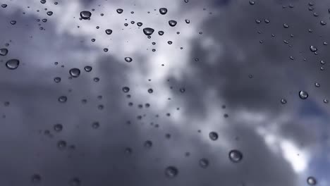 White-puffy-clouds-passing-by-in-the-blue-sky-with-sunlight-shining-through-with-rain-drops-on-a-glass-window-in-focus---HD-Time-lapse