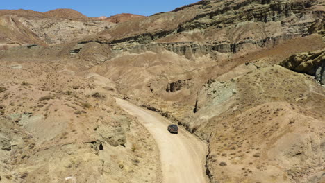 Ein-Dunkelschwarzer-Geländewagen-Steht-Am-Rand-Einer-Kurvigen-Unbefestigten-Straße-Durch-Das-Regenbogenbecken-In-Der-Mojave-Wüste