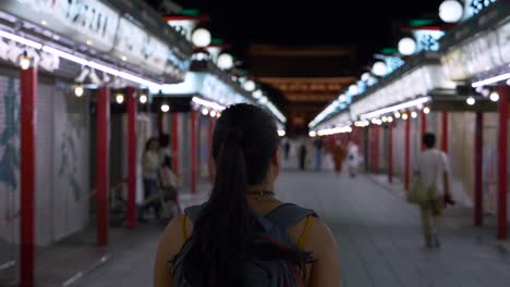 A-young-female-traveler-walking-towards-Sensoji-Temple,-in-slow-motion,-at-night-along-Nakamise-Shopping-Street-in-Asakusa,-Tokyo