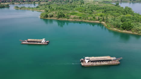 Barcos-Industriales-De-Transporte-De-Arena-Navegando-Lentamente-A-Lo-Largo-Del-Río-Con-árboles-En-El-Paseo-Marítimo