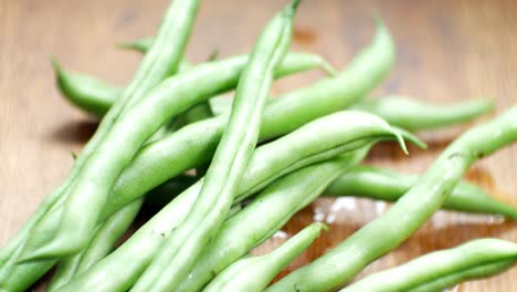 Hand-placing-raw-fresh-uncooked-string-beans-on-wooden-kitchen-surface-close-up-selective-focus