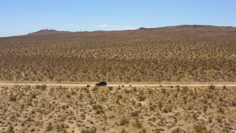 Black-SUV-speeds-quickly-down-a-perfectly-straight-road-through-the-plains-of-the-Mojave-Desert-on-a-clear-blue-day