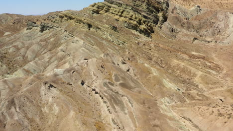 Vista-De-Drones-Volando-Sobre-Un-Camino-Curvo-Y-Sinuoso-Al-Pie-De-Montañas-Secas-Y-Formaciones-Geológicas-En-El-Desierto-De-Mojave