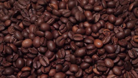 Dark-roast-coffee-beans-sprinkling-onto-solid-background-of-beans,-Slow-Motion